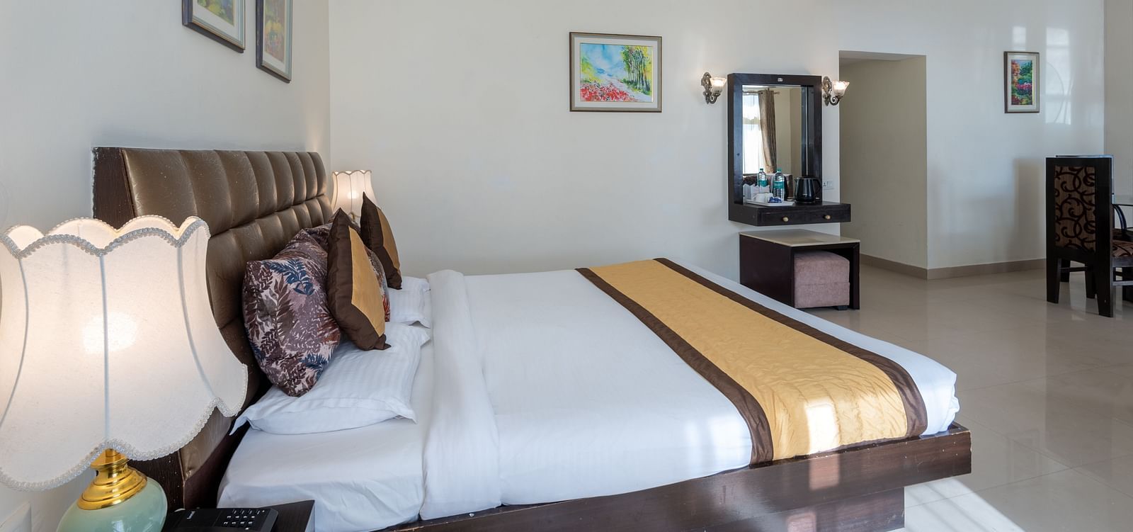 A spacious hotel room with a large bed, a dresser with a mirror, a lamp, and artwork on the walls | DLS The Pearl